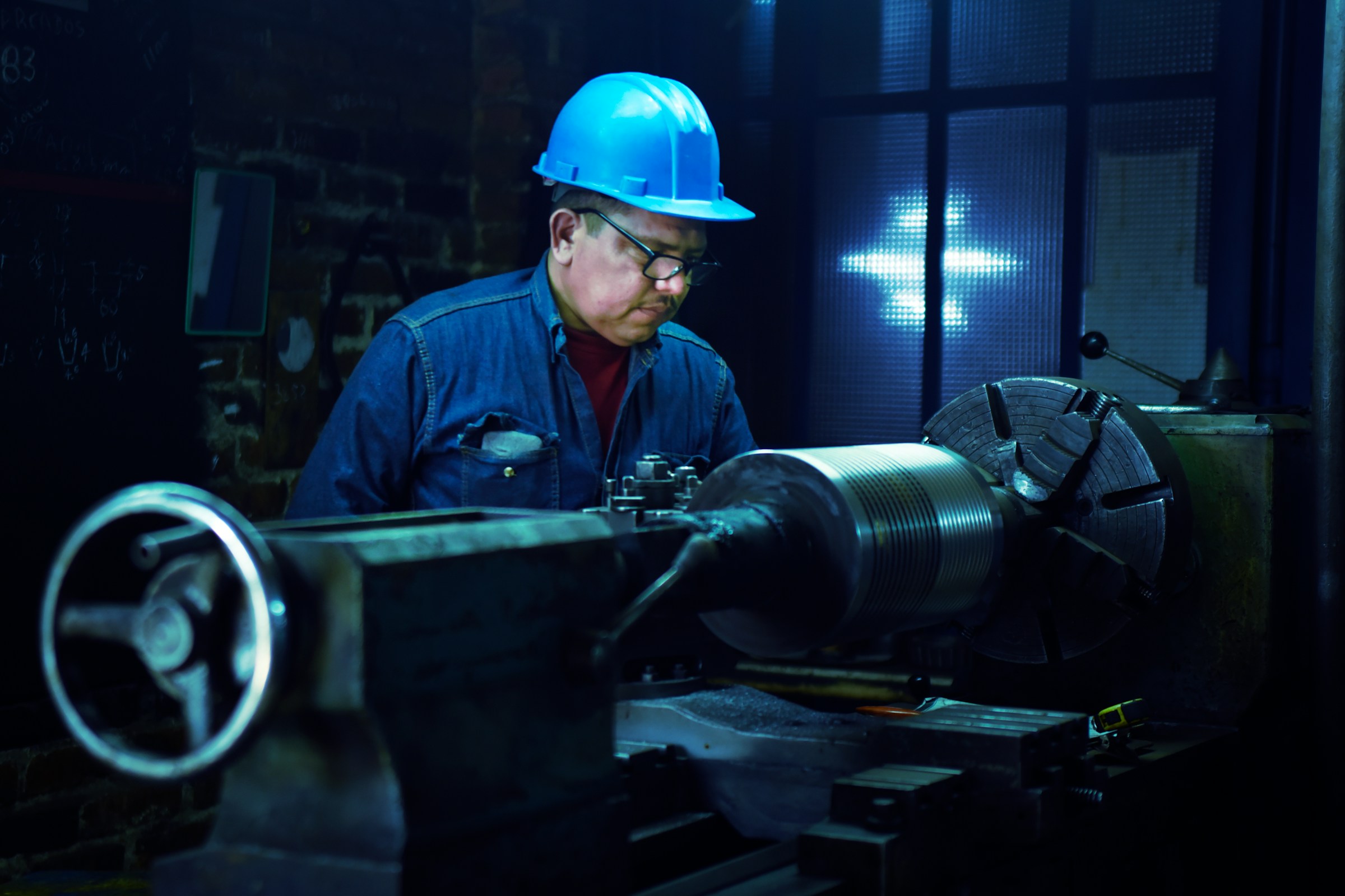 Machinist in a hard hat working a precision lathe on a shop floor