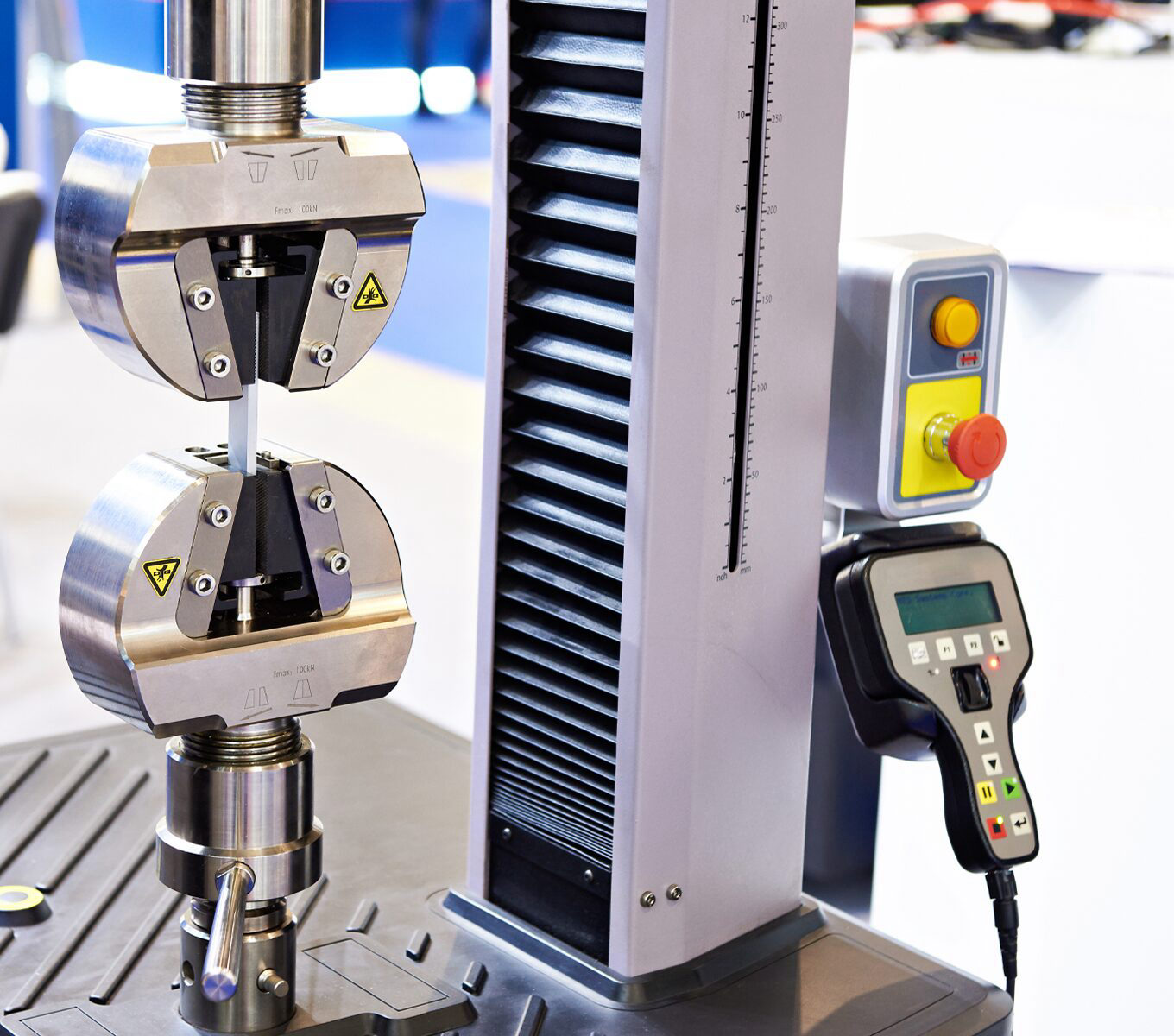 Universal testing machine with 100 kN wedge grips extending a metal specimen, hand pendant alongside