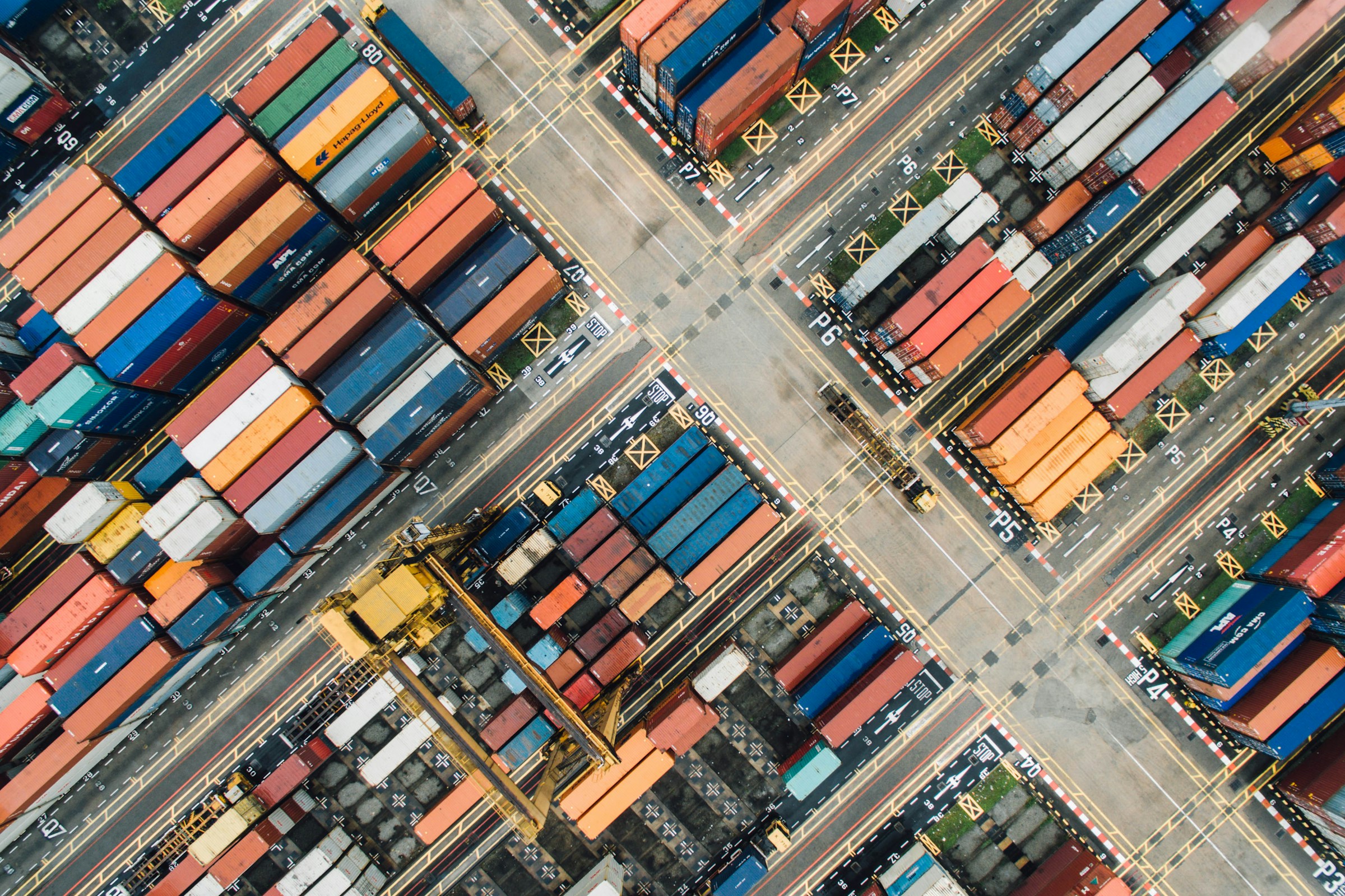 Aerial view of stacked shipping containers and gantry cranes at a port terminal