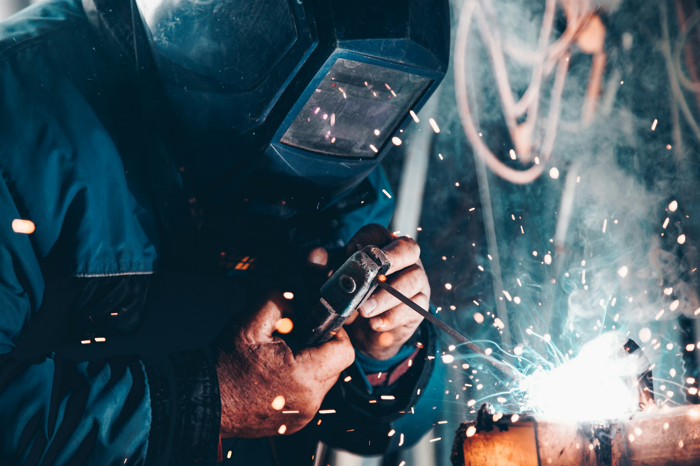 Welder in a protective mask joining steel, sparks flying from the arc