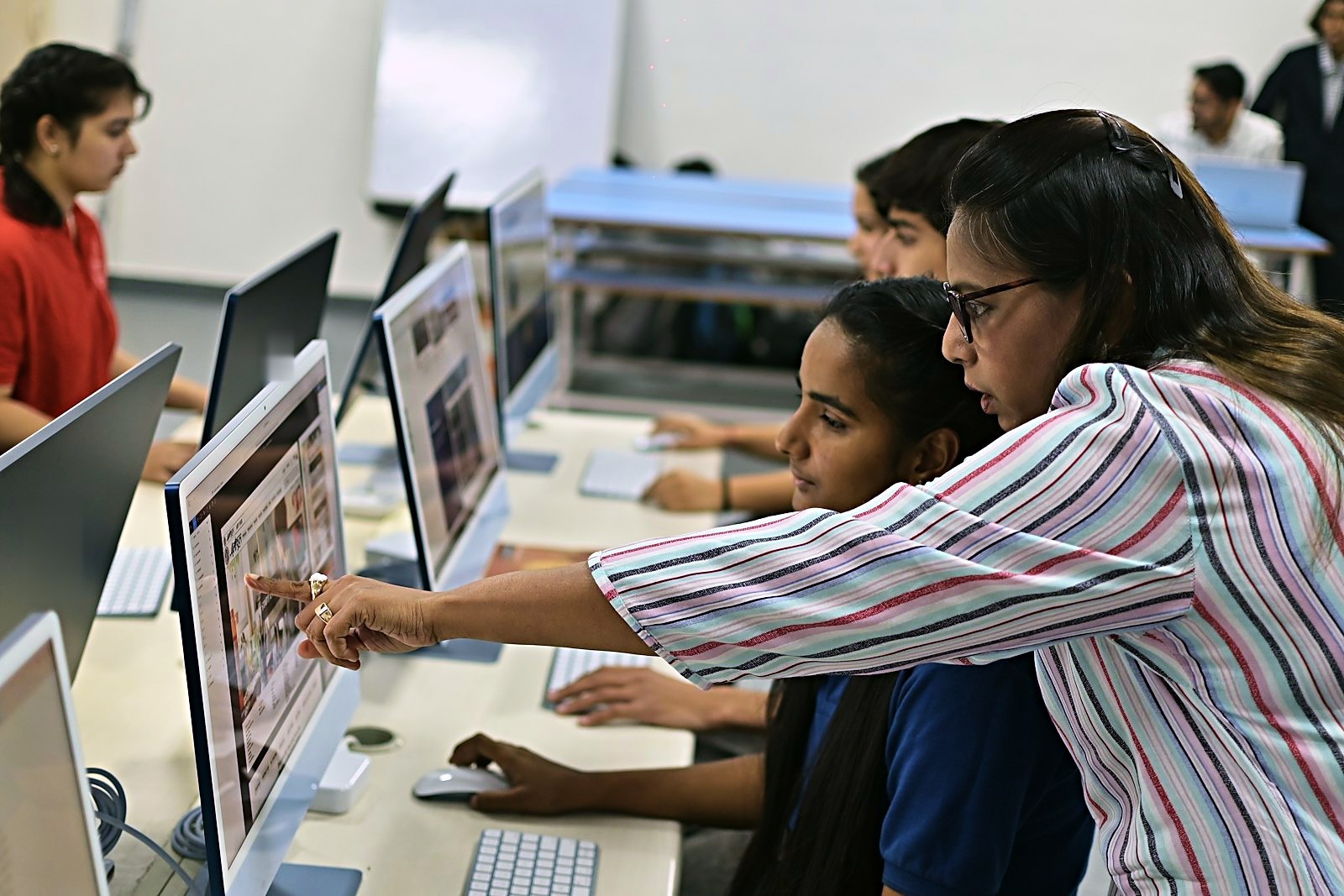 Instructor guiding students at a row of desktop computers in a college lab