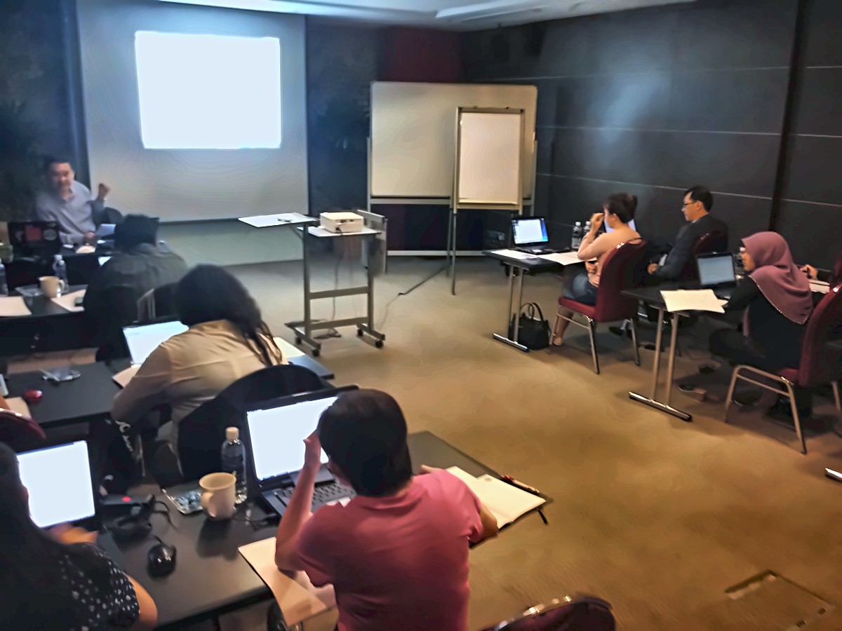 Participants at laptops during a management training session with a facilitator and projector