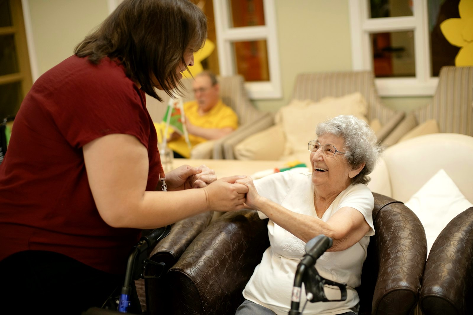 Care worker helping an elderly resident up from an armchair in a care home lounge